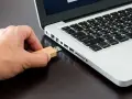 Mano inserisce una chiavetta USB in un laptop, pronta per formattare.