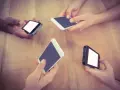 Mani che tengono smartphone su un tavolo di legno, forse in attesa di un segnale Vodafone in Inghilterra.