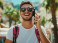 Giovane sorridente al telefono, con uno zaino a quadri rossi. Forse sta parlando con operatori telefonici in Canada, godendosi il sole.