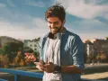 Giovane sorridente con smartphone e cuffie, impara come telefonare dall'estero in Italia con il cellulare.