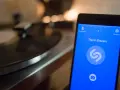 Smartphone con app Shazam aperta, pronto a identificare un brano. Sullo sfondo, un giradischi vintage.