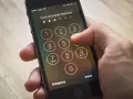 Dito si vede come sbloccare iPhone inserendo il codice. La mano preme i tasti numerici sullo schermo.