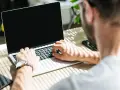 Uomo al lavoro su un laptop, monitora la temperatura CPU. Luce solare filtra attraverso le persiane.