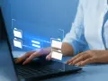 Mani su tastiera laptop, interfaccia digitale con icone di cartelle e frecce che indicano il trasferimento dati, utile per capire come inviare video pesanti.