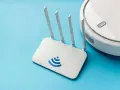 Un router Wi-Fi bianco con logo blu e un robot aspirapolvere bianco su sfondo azzurro. Cos'è un router? È il cuore della tua connessione internet.