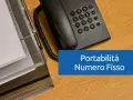 Telefono fisso e documenti su scrivania in legno. Testo: "Portabilità Numero Fisso".