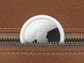 Un AirTag Apple sporge da una cerniera di una borsa in pelle marrone. Scopri airtag come funziona per ritrovare i tuoi oggetti.