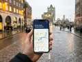 Mano che tiene uno smartphone con mappa di Londra e connessione 5G, sullo sfondo una strada bagnata e palazzi caratteristici.