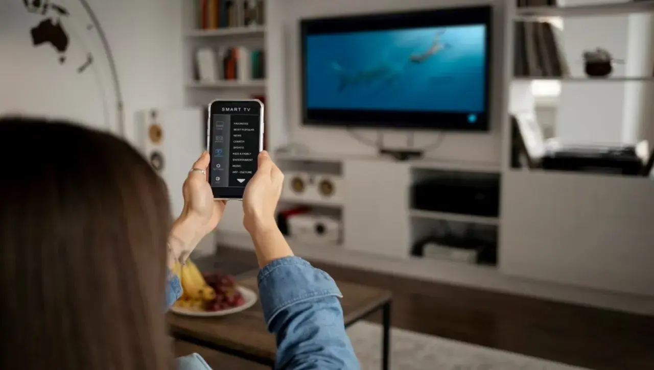 Una persona usa il suo smartphone per controllare la Smart TV, mostrando come collegare il telefono alla tv per un'esperienza di intrattenimento domestico.