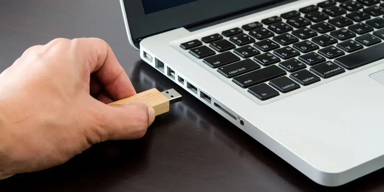 Mano inserisce una chiavetta USB in un laptop, pronta per formattare.