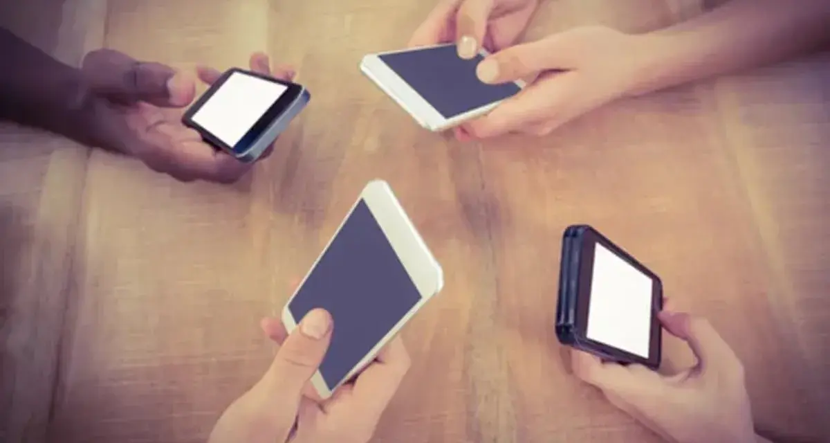 Mani che tengono smartphone su un tavolo di legno, forse in attesa di un segnale Vodafone in Inghilterra.