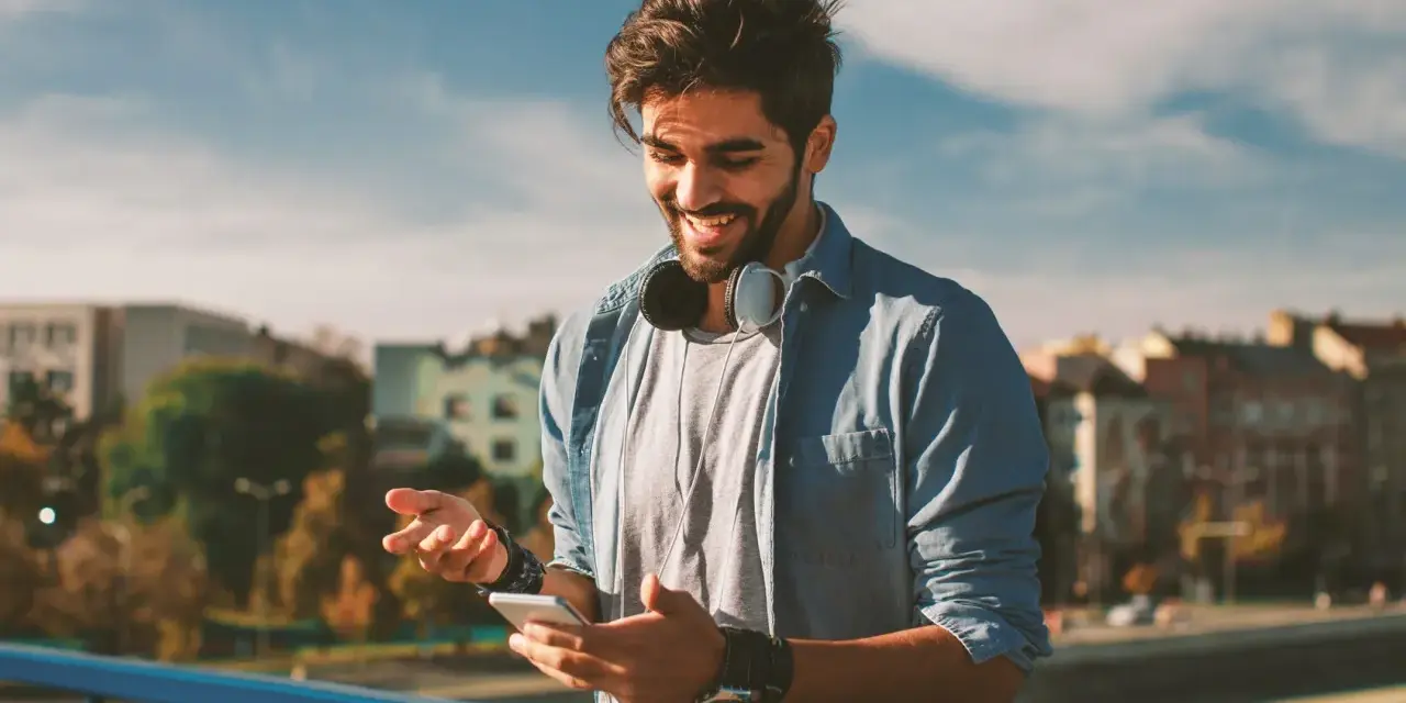 Giovane sorridente con smartphone e cuffie, impara come telefonare dall'estero in Italia con il cellulare.