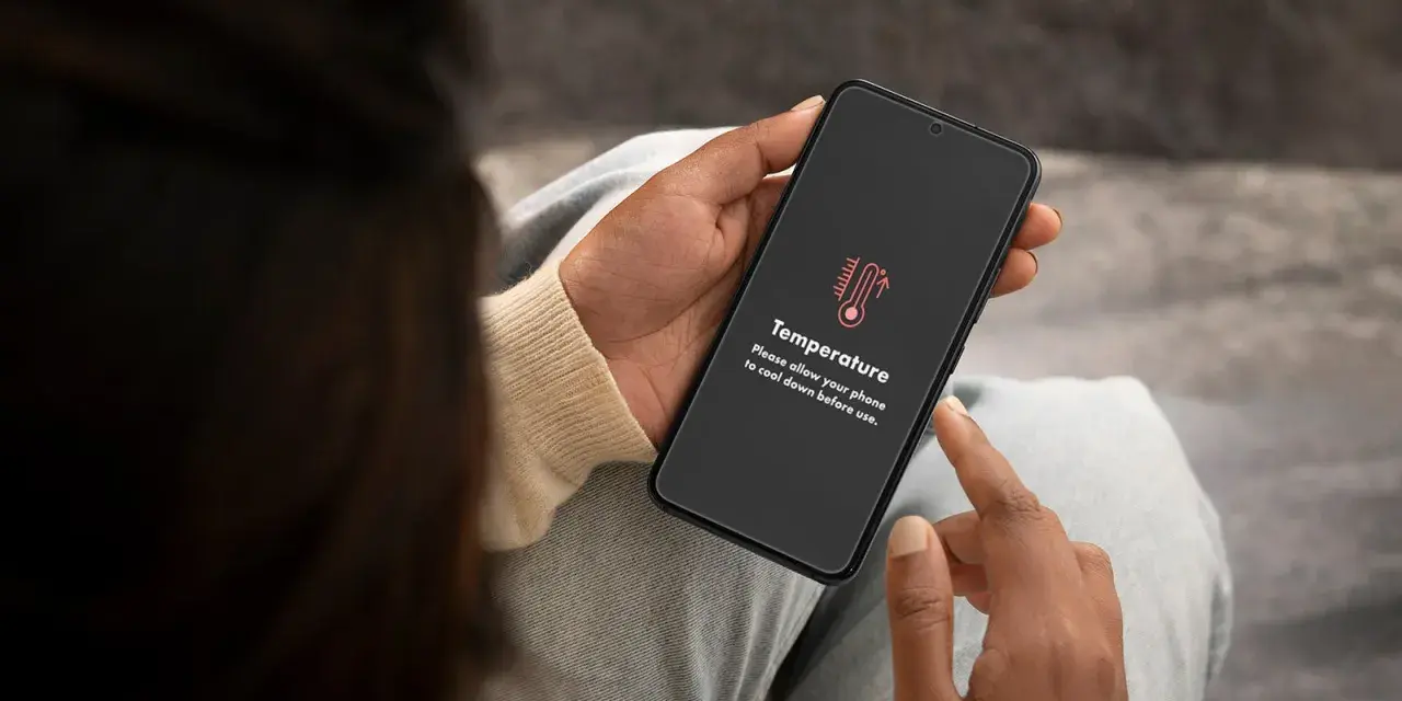 Mani che tengono uno smartphone con un messaggio di avviso "Temperatura". È ora di capire come raffreddare il telefono.