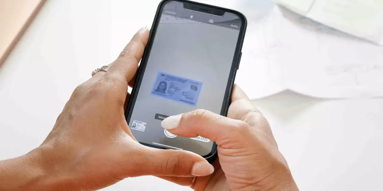 Mani che usano uno smartphone per scannerizzare un documento d'identità. L'app mostra un'anteprima del documento.