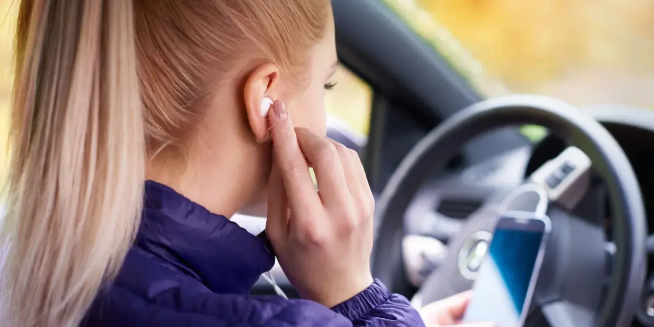 Ragazza in auto inserisce auricolari, pronta per ascoltare musica o chiamare. Come togliere la e sul cellulare? Forse sta cercando un modo per disattivare le notifiche.