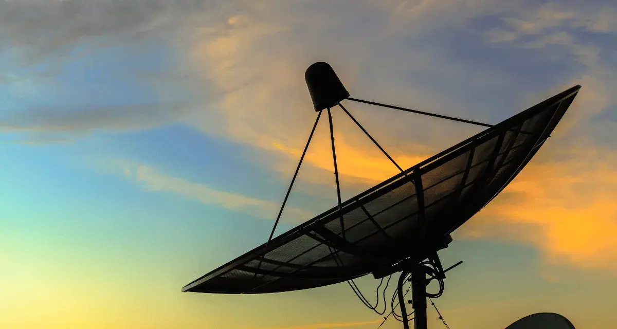 Antenna parabolica in controluce al tramonto, pronta a connettersi al mondo tramite internet satellitare.