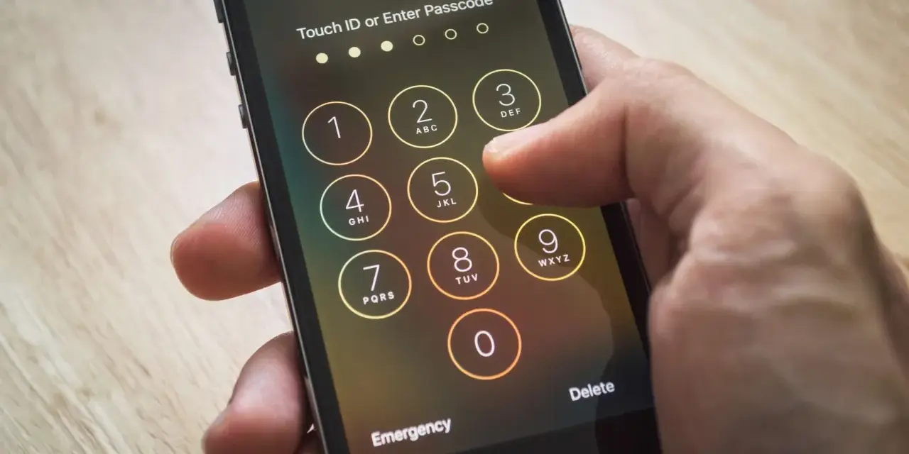 Dito si vede come sbloccare iPhone inserendo il codice. La mano preme i tasti numerici sullo schermo.