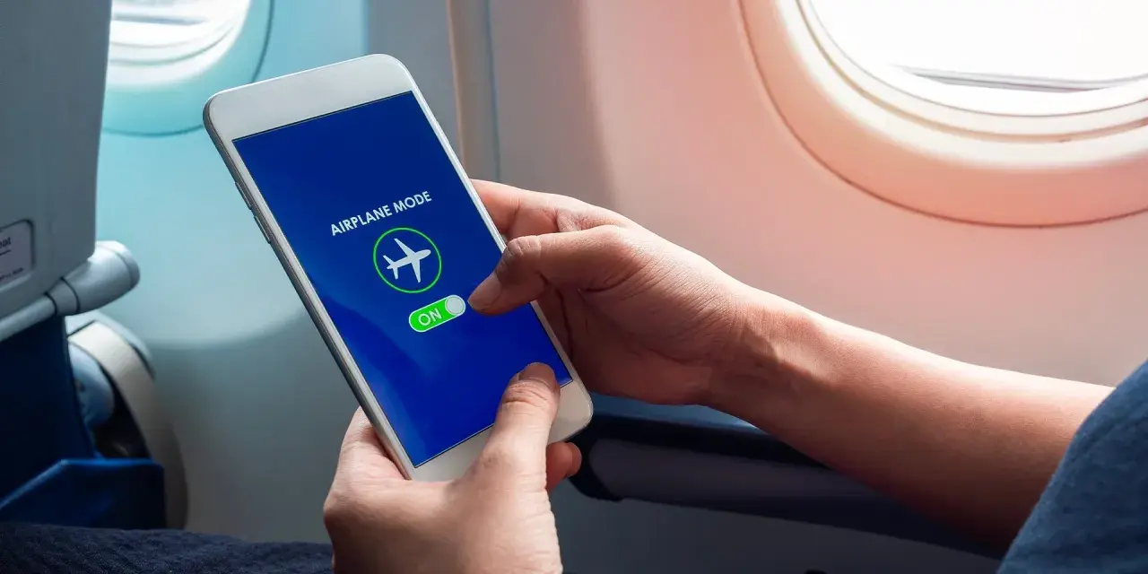 Mani che attivano la modalità aereo sul telefono, seduti vicino al finestrino di un aereo.