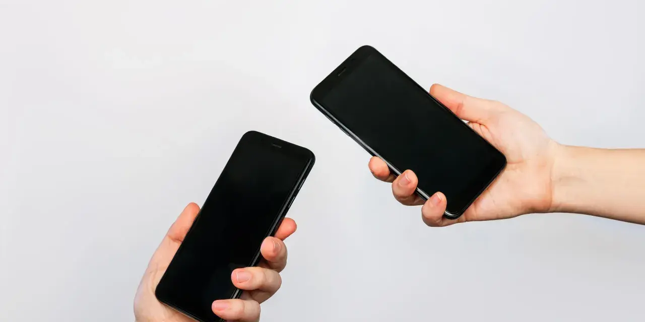 Due mani tengono due smartphone neri, uno in primo piano e uno più lontano, illustrando come trasferire i dati da un telefono all'altro.
