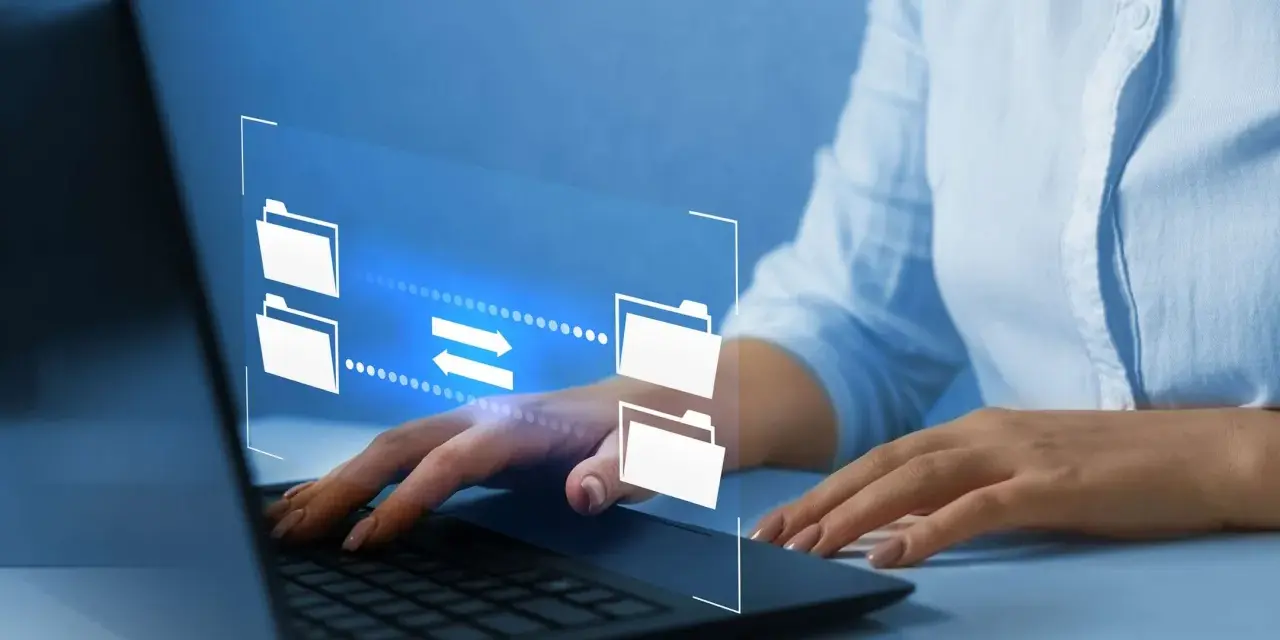 Mani su tastiera laptop, interfaccia digitale con icone di cartelle e frecce che indicano il trasferimento dati, utile per capire come inviare video pesanti.