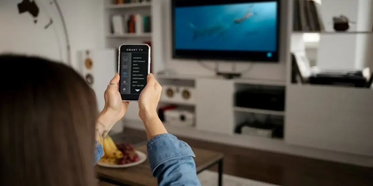 Una persona usa il suo smartphone per controllare la Smart TV, mostrando come collegare il telefono alla tv per un'esperienza di intrattenimento domestico.