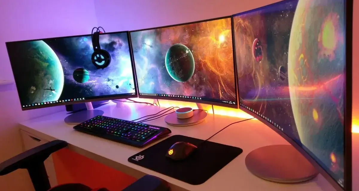 Postazione gaming con tre monitor curvi che mostrano pianeti spaziali. La tastiera e il mouse sono illuminati, pronti per ruotare schermo pc e immergersi nell'avventura.