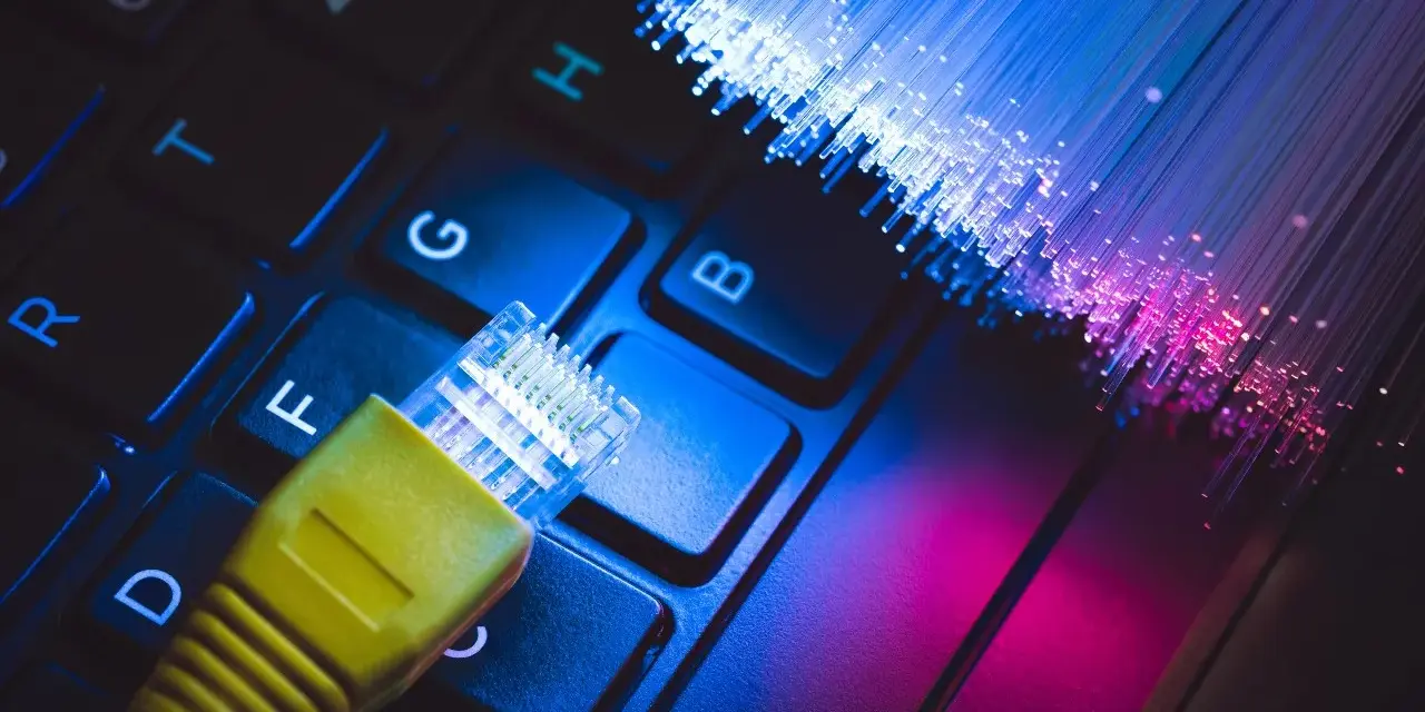 Connessione internet: un cavo giallo su tastiera e fibre ottiche luminose. Capire cos'è l'ADSL è fondamentale per la tua navigazione.