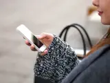Mano che tiene uno smartphone, con un maglione a trecce e una borsa sullo sfondo. La persona sta utilizzando dati per navigare.