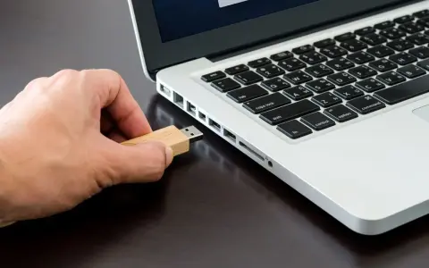 Mano inserisce una chiavetta USB in un laptop, pronta per formattare.
