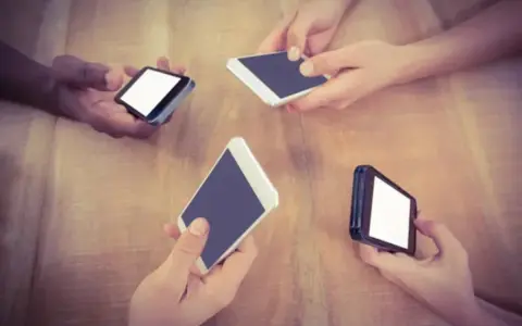Mani che tengono smartphone su un tavolo di legno, forse in attesa di un segnale Vodafone in Inghilterra.