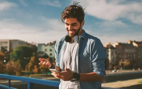 Giovane sorridente con smartphone e cuffie, impara come telefonare dall'estero in Italia con il cellulare.