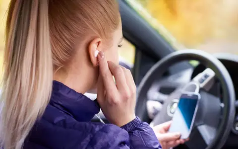 Ragazza in auto inserisce auricolari, pronta per ascoltare musica o chiamare. Come togliere la e sul cellulare? Forse sta cercando un modo per disattivare le notifiche.