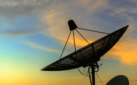 Antenna parabolica in controluce al tramonto, pronta a connettersi al mondo tramite internet satellitare.