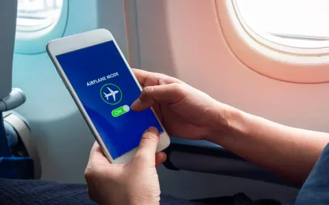 Mani che attivano la modalità aereo sul telefono, seduti vicino al finestrino di un aereo.