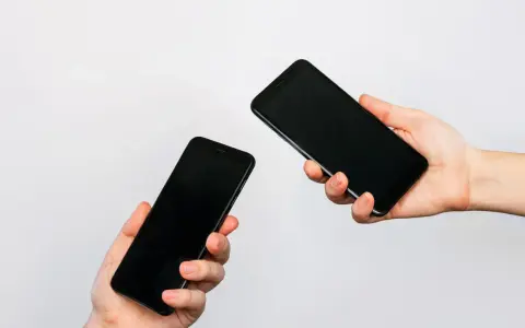 Due mani tengono due smartphone neri, uno in primo piano e uno più lontano, illustrando come trasferire i dati da un telefono all'altro.