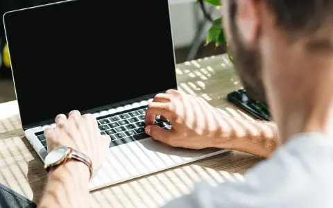 Uomo al lavoro su un laptop, monitora la temperatura CPU. Luce solare filtra attraverso le persiane.