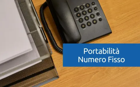 Telefono fisso e documenti su scrivania in legno. Testo: "Portabilità Numero Fisso".