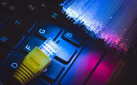 Connessione internet: un cavo giallo su tastiera e fibre ottiche luminose. Capire cos'è l'ADSL è fondamentale per la tua navigazione.