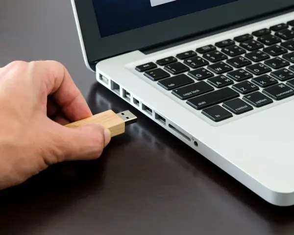 Mano inserisce una chiavetta USB in un laptop, pronta per formattare.