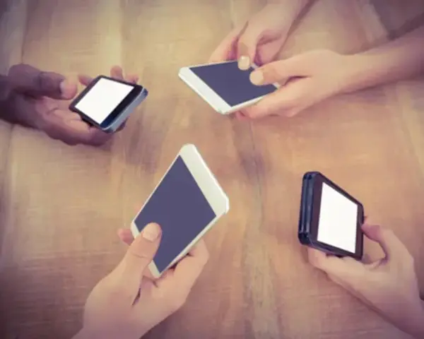 Mani che tengono smartphone su un tavolo di legno, forse in attesa di un segnale Vodafone in Inghilterra.