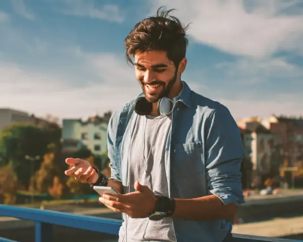 Giovane sorridente con smartphone e cuffie, impara come telefonare dall'estero in Italia con il cellulare.