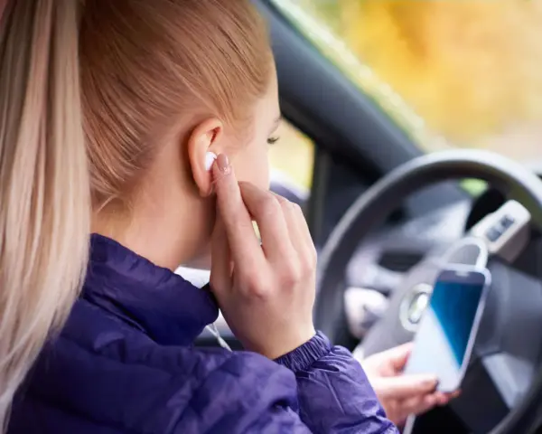 Ragazza in auto inserisce auricolari, pronta per ascoltare musica o chiamare. Come togliere la e sul cellulare? Forse sta cercando un modo per disattivare le notifiche.