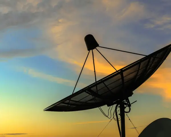 Antenna parabolica in controluce al tramonto, pronta a connettersi al mondo tramite internet satellitare.