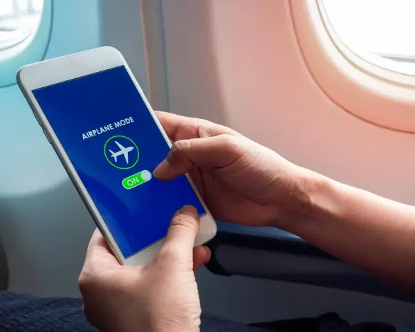 Mani che attivano la modalità aereo sul telefono, seduti vicino al finestrino di un aereo.