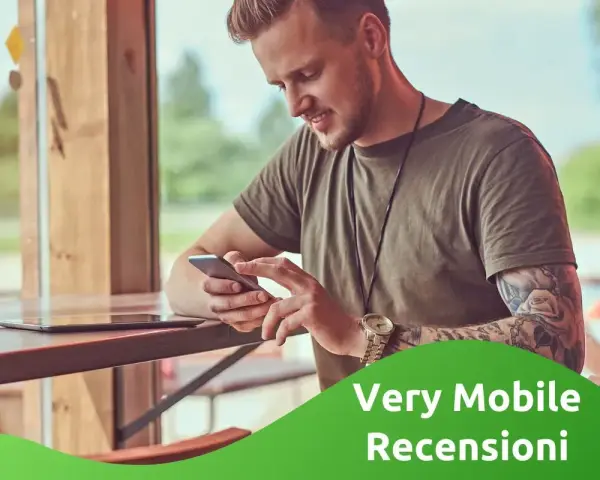 Uomo con tatuaggi guarda il suo smartphone, leggendo le very opinioni su "Very Mobile Recensioni".
