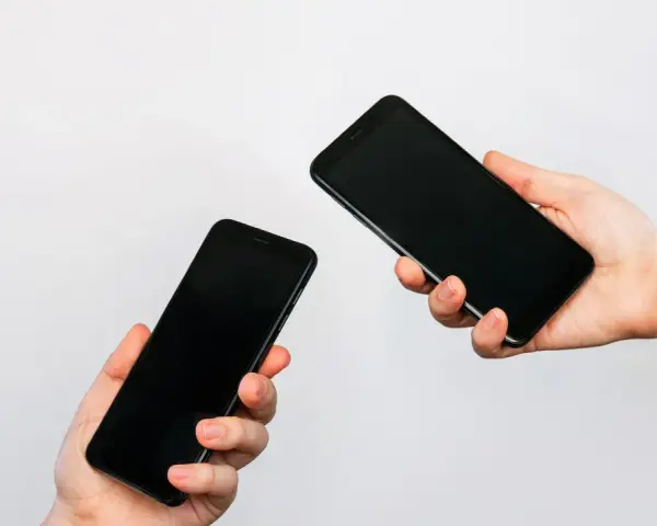 Due mani tengono due smartphone neri, uno in primo piano e uno più lontano, illustrando come trasferire i dati da un telefono all'altro.