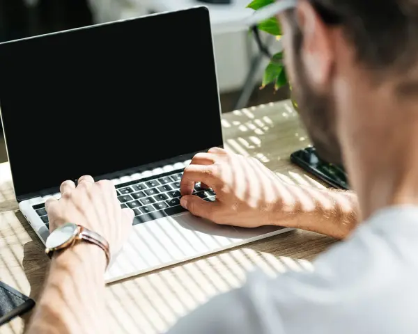 Uomo al lavoro su un laptop, monitora la temperatura CPU. Luce solare filtra attraverso le persiane.