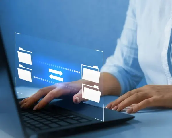 Mani su tastiera laptop, interfaccia digitale con icone di cartelle e frecce che indicano il trasferimento dati, utile per capire come inviare video pesanti.