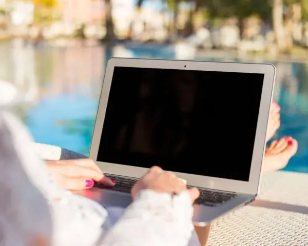 Donna lavora al laptop vicino alla piscina, godendosi l'internet temporaneo per la seconda casa.