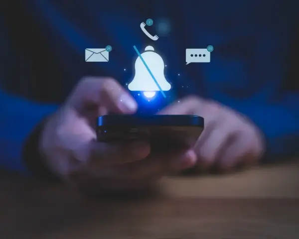 Mani che tengono uno smartphone, con icone di notifiche (email, messaggi, chiamate) e una campana barrata, per illustrare come silenziare le notifiche.